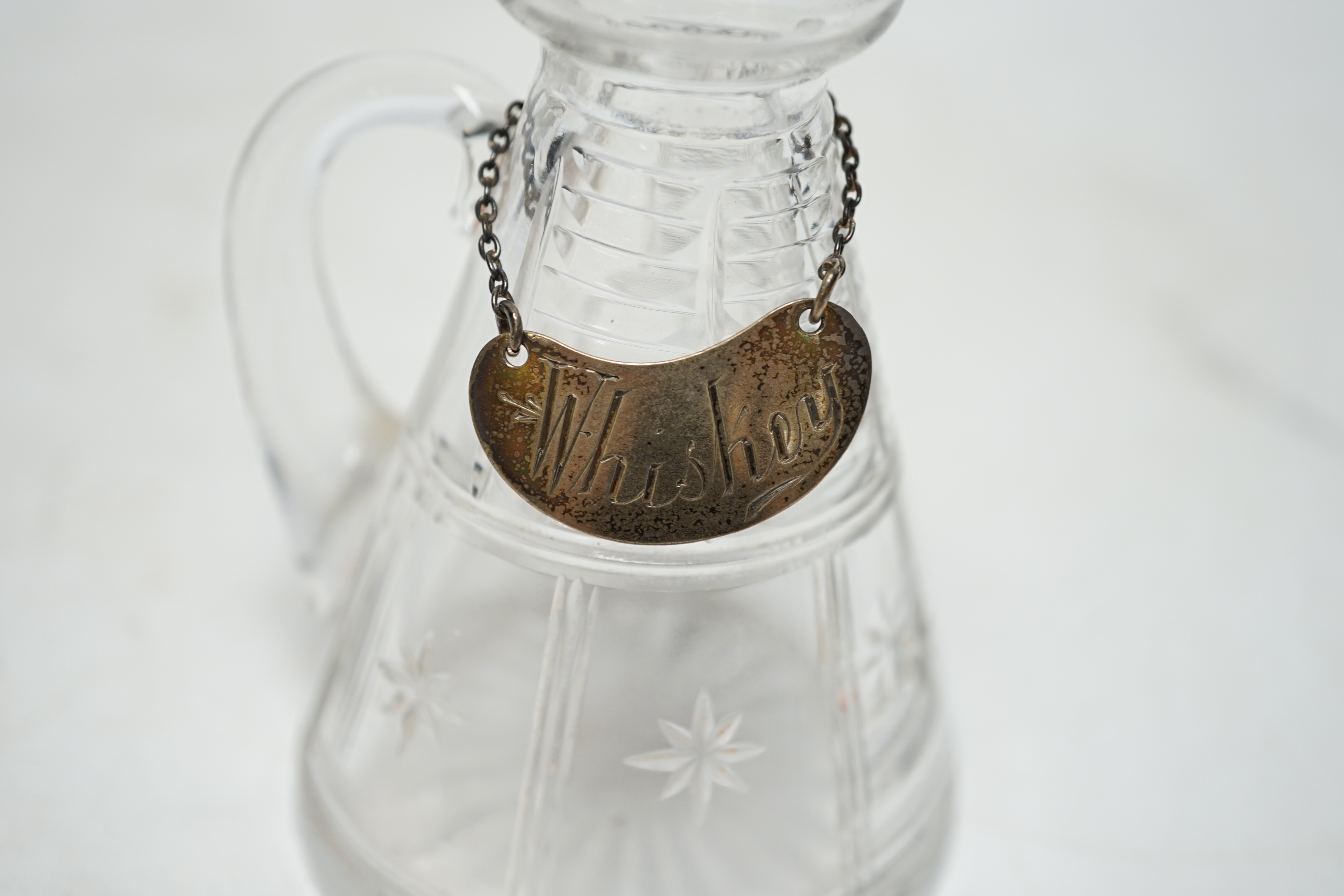 A George V silver mounted cut glass whisky noggin, Goldsmiths & Silversmiths Co Ltd, London, 1933, 10.9cm, with an Edwardian silver 'Whisky' wine label. Condition - poor